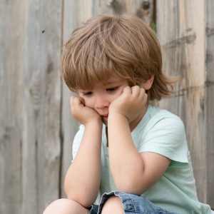 Sadness. Sad Boy. A Lonely Child Sits Near A Wooden Fence. Frust