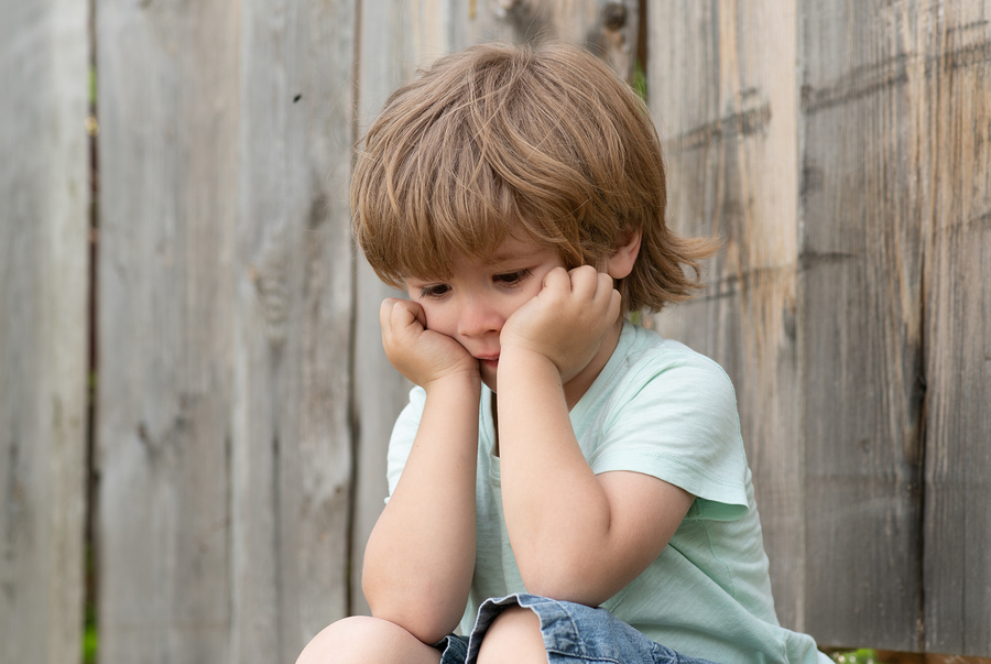 Sadness. Sad Boy. A Lonely Child Sits Near A Wooden Fence. Frust